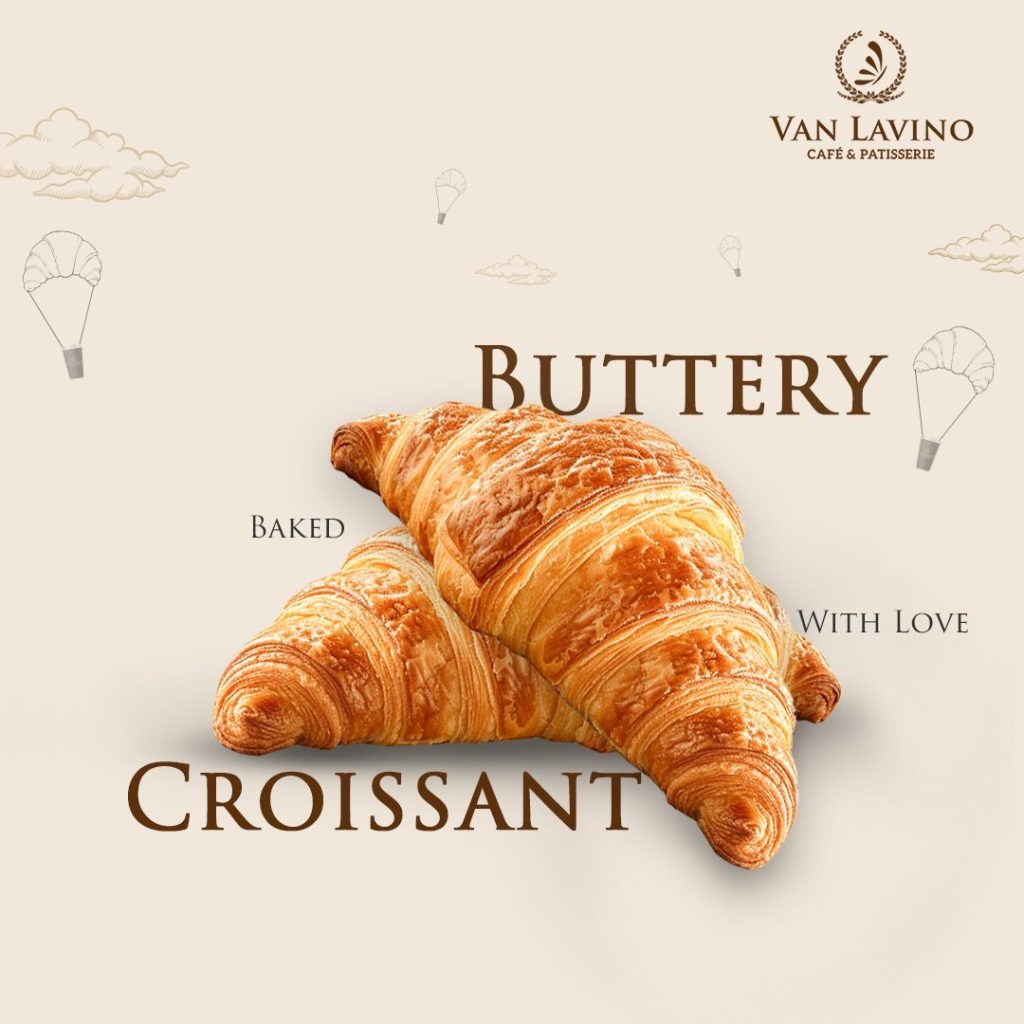 A golden, flaky croissant with delicate layers, served on a white plate alongside a steaming cup of cappuccino.